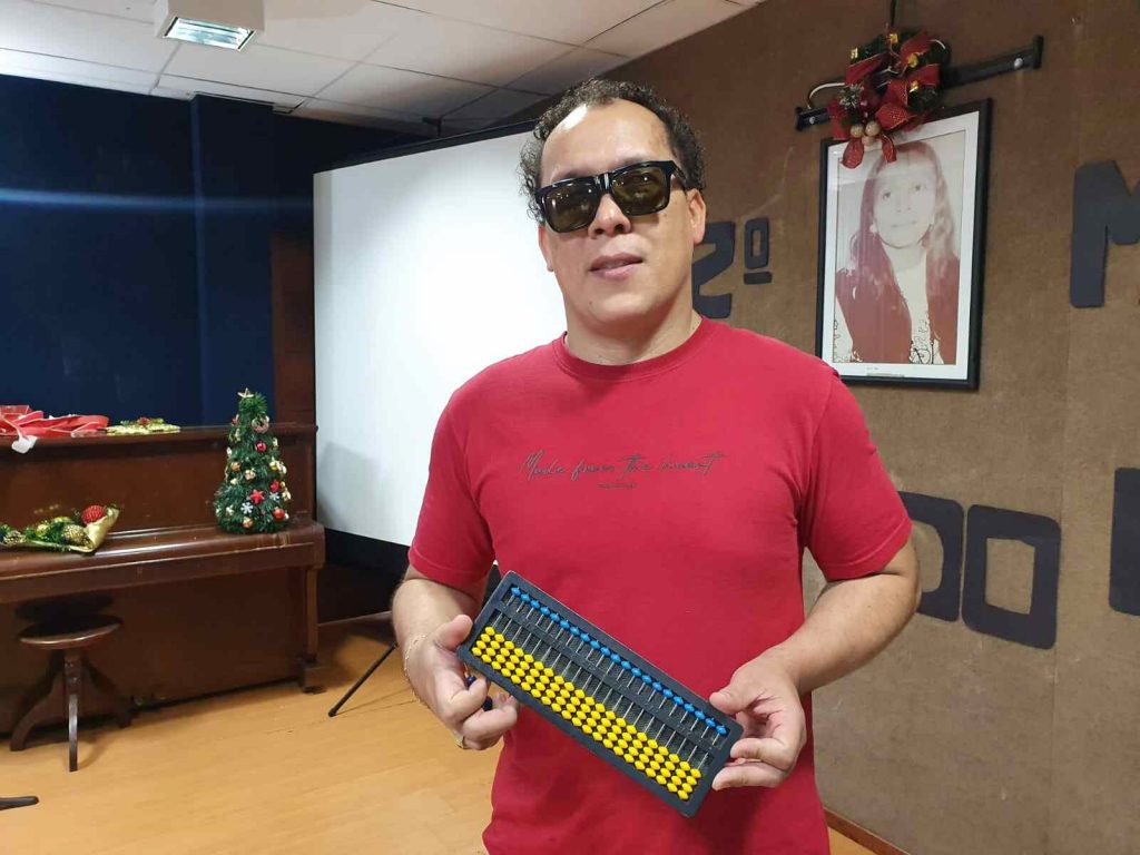 Márcio Ximenez, presidente do Ismac, vestido com camiseta vermelha e com soroban em mãos 