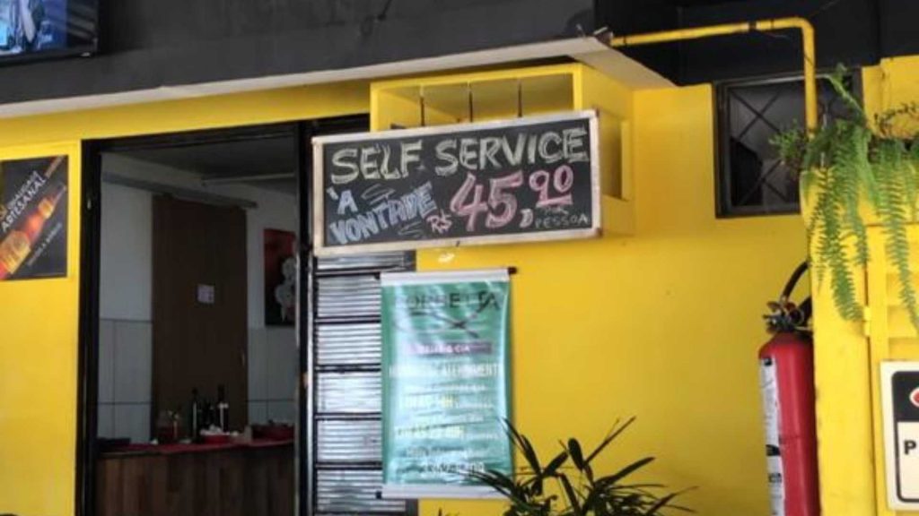 Área interna da peixaria, de cor amarela, e placa escrita com giz com o valor de R$ 45,90 o self-service à vontade.